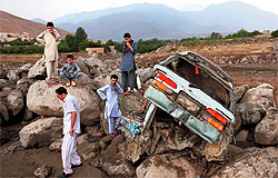 Afghans stand near a destroyed car after floods in Kabul on Sunday