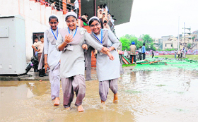 Schoolchildren remove their shoes and wade through water accumulated on the ground in Amritsar on Monday.