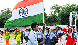 A youth carries the National Flag as other schoolchildren salute during the full dress rehearsal for the Independence Day function at Parade Ground in Sector 17, Chandigarh, on Tuesday