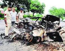 Police personnel inspect the burnt car near Kundli on the GT Road on Tuesday. 