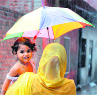 A woman protects herself and her child from rain by using an umbrella in Amritsar on Friday.