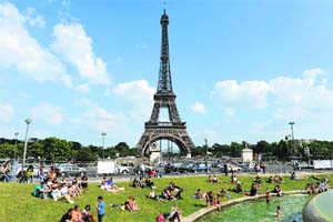 Children play in a fountain while people enjoy the sun in front of the Eiffel Tower.