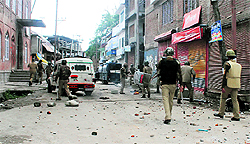 Security forces personnel walk through the street strewn with stones thrown by protesters agitating against the alleged desecration of the holy book in Shopian on Sunday