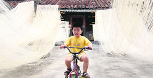 A boy rides a bicycle in between homemade noodles in the Fujian province of China.