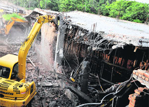 A JCB machine razes illegally-constructed shops on the Waqf Board land near the Grain Market in Bathinda on Tuesday.