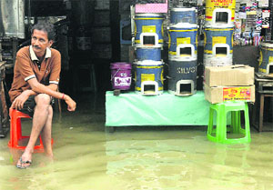 A shopkeeper sits outside a shop on a waterlogged road in Kolkata on Wednesday.