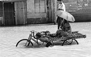 A boy carries passengers on his rickshaw wading through flood water at Ghatal in West Midnapore district on Thursday.