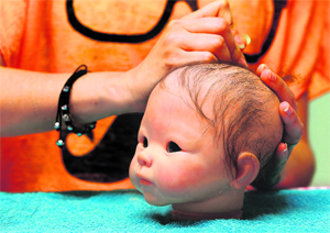 Artist Landeghem uses a needle to attach hair to the head of one of her dolls.