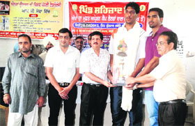 Basketball player Satnam Singh receives the revolving trophy of the project Health for All from office-bearers of Punarjot Eye Bank Society during the launch of National Eye Donation Awareness Fortnight at Sehzad village on Tuesday