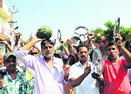Vijay Kumar, former MC, carries vegetables while residents bang utensils to raise their voice against the rising inflation at Paras Ram Nagar in Bathinda on Wednesday.