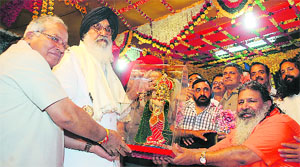 Punjab Chief Minister Parkash Singh Badal receives an idol of Lord Krishna from Baba Bal at Kotla Kalan in Una district on Thursday. 
