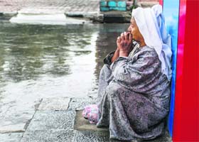An elderly woman outside a shop amid the rains