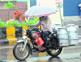  A milkman carries an umbrella while riding a motorcycle to protect himself from rain in Amritsar on Monday