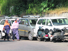 Women walk past the vehicles parked on a roadside.