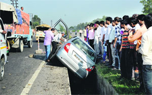 Commuters look at a car that got stuck in an open drain on the NH-1 near the Jalandhar bypass on Tuesday.