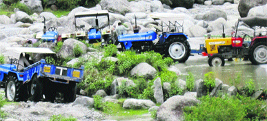 Tractor-trailers extract stones from the Neugal river, near Palampur.