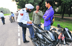 Traffic police personnel challan offenders at Sector 9; and (below) a youth rides a two-wheeler without wearing a helmet at Sector 10 in Chandigarh. Tribune photos: Pradeep Tewari