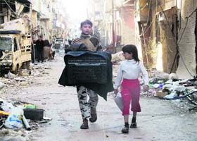 Caught in conflict: Children carry their possession while walking past damaged buildings in Holms city of Syria on Sunday