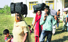 Villagers of Suchetgarh-Kulian shift with their belongings to Kalibari village in Samba district on Saturday. (Below) The villagers take refuge in a community hall in Kalibari village.
