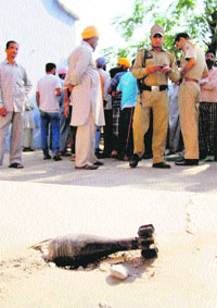 Villagers and policemen stand near an unexploded mortar shell fired by Pakistani troops at Jerda village in Ramgarh sector of Samba district on Monday. 