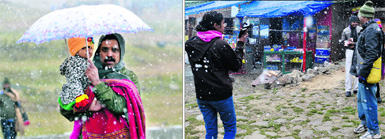 A father with his child enjoys the snowfall; and (right) tourists click photographs in Gulmarg on Thursday.