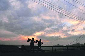 Two workers walk under dark clouds at sunset in Shimla on Tuesday