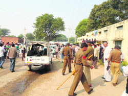 Policemen keep a watch as villagers protest against the rape of a schoolgirl at Nigana Kalan village in Bhiwani, Haryana, on Saturday.