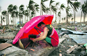 A man uses an umbrella as a shelter against the wind as he tries to light a fire amid the rubble at Tacloban in Philippines on Thursday.
