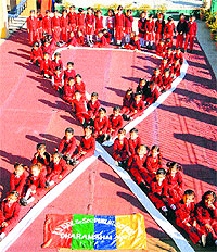 Students of DAV Public School stand in the shape of a red ribbon on the eve of World AIDS Day at Dharamsala on Saturday