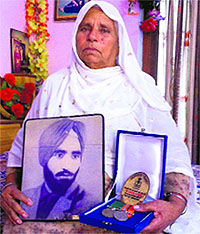 Manjit Kaur, wife of Har Kisahn Singh with the photograph of her husband, who is a prisoner of war, and his medals
