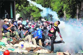 An anti-government protester throws a tear gas shell back at the riot police in Bangkok on Monday