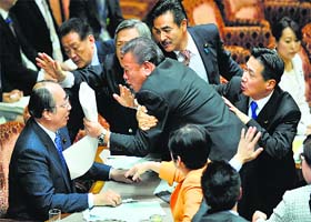 Free for all: Lawmakers of opposition parties try to disrupt proceedings as Masaharu Nakagawa, chairman of the upper house special committee, announces the approval of a new secrecy law in Tokyo on Thursday