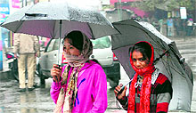 Girls walk with umbrellas in the first rain of the winter at Clock Tower in Dehradun on Sunday