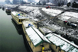 Snow-covered houseboats lined up along the banks of the Jhelum