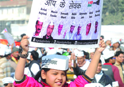 A child, supporter of the Aam Aadmi Party, holds a poster of ministers who took oath during the swearing-in ceremony in New Delhi on Saturday. Tribune photo: Mukesh Aggarwal