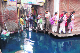 Schoolchildren take the help of benches to cross a street submerged with sewerage water at Hansli Wali Gali in Amritsar.