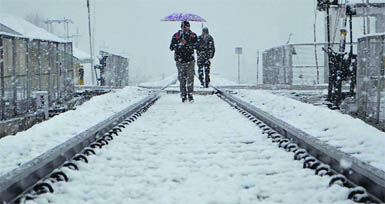 A man walks under an umbrella on the snowbound railway track near Anantnag in South Kashmir on Wednesday