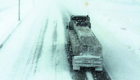 A truck moves cautiously through blowing snow.