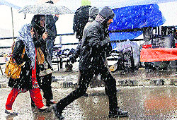 Pedestrians protect themselves with an umbrella during a fresh snowfall in Srinagar on Wednesday