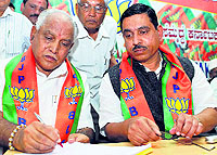 Former Karnataka Chief Minister BS Yeddyurappa signs papers as BJP state president Prahalad Joshi looks on, in Bangalore