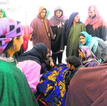 Women encircle Ayesha Begum (under the blanket) while she delivers a baby in the open at Kukroosa village in Handwara.