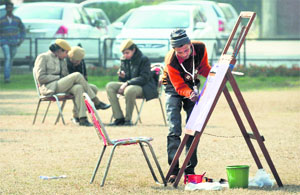 An artist gives finishing touches to his work, while police personnel relax in the background.
