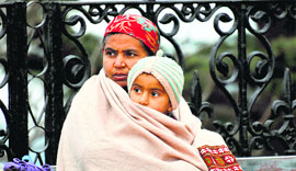 A woman wraps herself and her child under a shawl to beat the chill on The Ridge in Shimla on Friday.