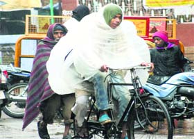 A man covers himself with a plastic sheet during a rainy and cold day in Varanasi on Saturday