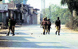 Pakistani policemen and army soldiers stand guard over a road leading to the site of bomb explosion in Bannu on Sunday