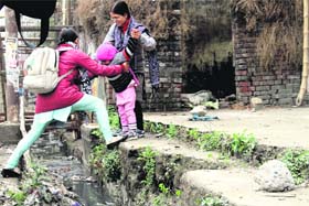 A woman takes the help of a passerby to cross a drain along with her child at the Rispana bridge barricading near the Vidhan Sabha in Dehradun