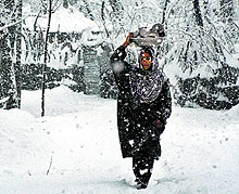 A Kashmiri woman carries utensils as she walks down a snow-covered road in Anantnag on Wednesday