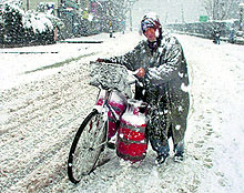 Braving cold weather conditions, a man carries cylinders on his bicycle as he walks on the banks of Dal Lake
