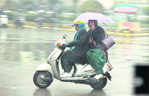 A woman drives a scooter while the pillion rider holds an umbrella to protect themselves from rain in Jalandhar on Wednesday.