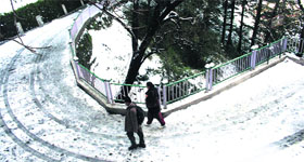 People walk on snow-covered road after fresh snowfall in Shimla on Thursday.